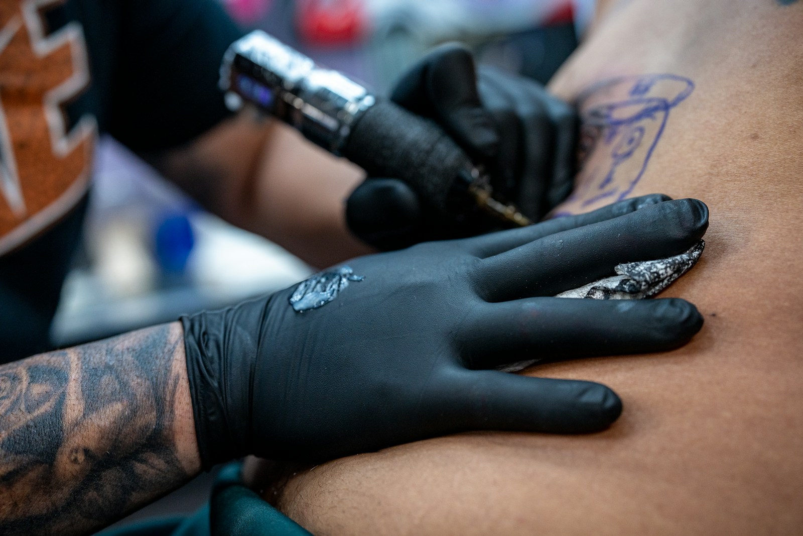 Tatuador con guantes negros trabajando con la máquina sobre la piel de un cliente